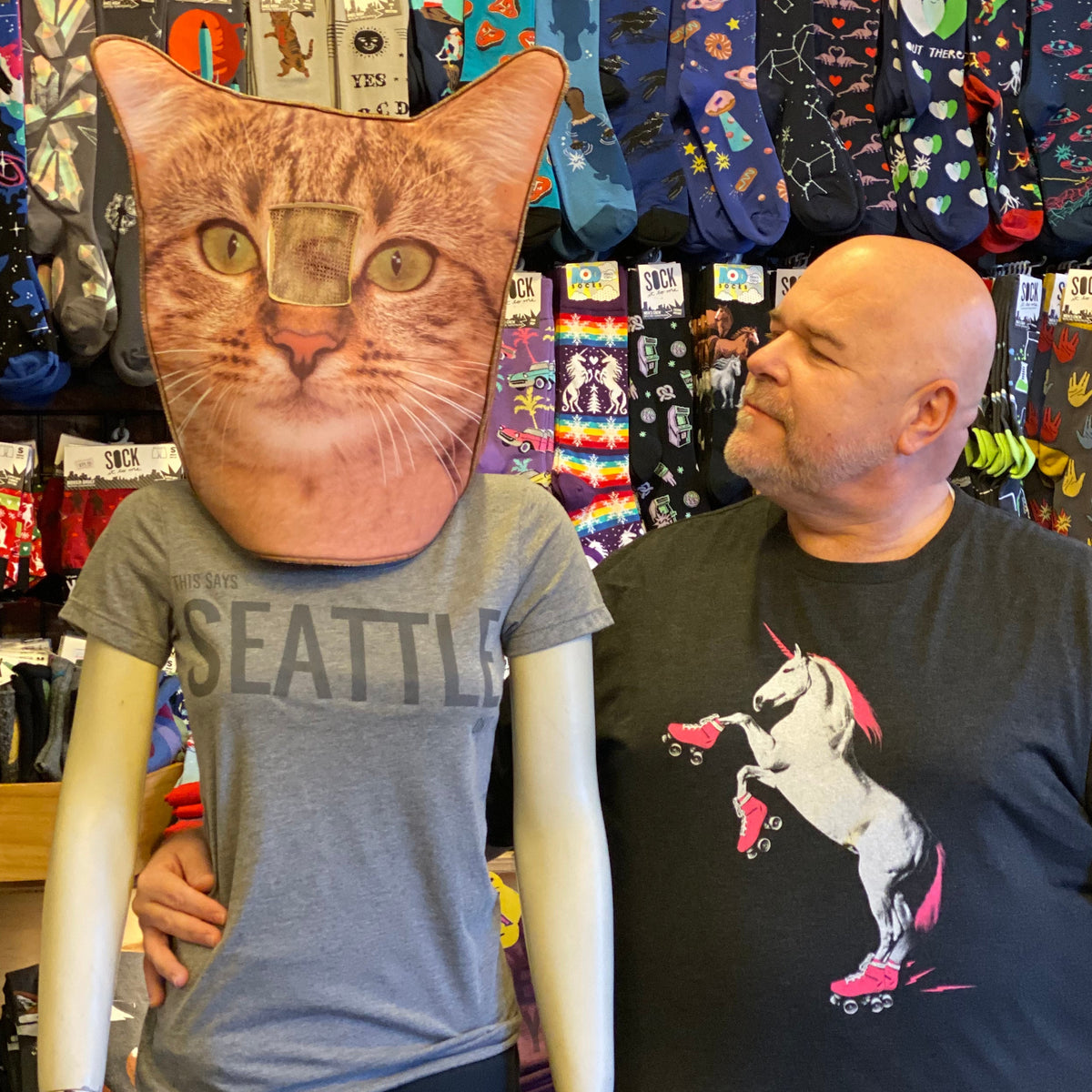 Person wearing a black t-shirt with a cat design, standing next to a display of colorful socks.