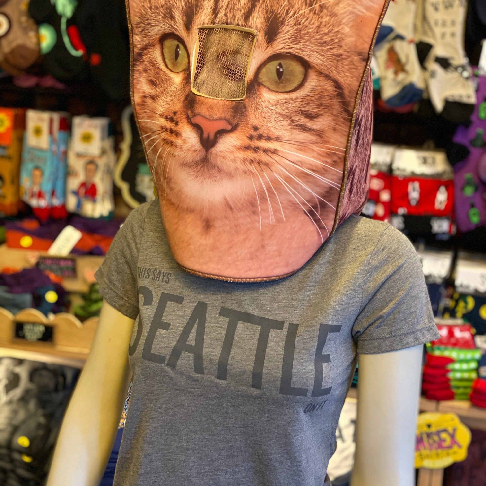 Mannequin wearing a cat face mask with a colorful store background. The shirt they are wearing is gray and it says "This Says Seattle On it." The perfect souvenir.