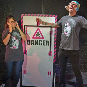 Two people in front of a 'DANGER' sign with a skull and crossbones symbol. They are both wearing astronaut unicorn shirts.