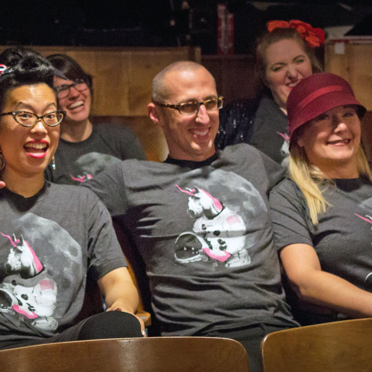 Group of people sitting together wearing matching gray t-shirts with a graphic design.