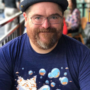 Man wearing a blue t-shirt with a graphic cat design, sitting in a casual setting.