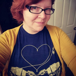 Person wearing a navy blue t-shirt with a heart design and yellow cardigan indoors.