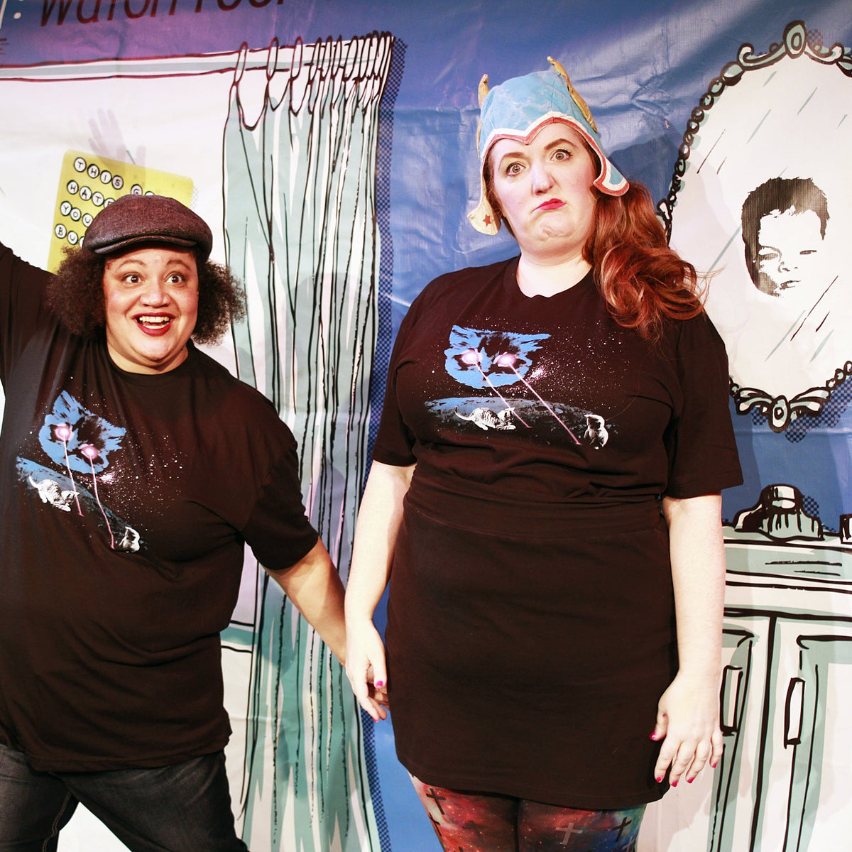 Two people wearing matching black t-shirts with a graphic design in front of a colorful backdrop.