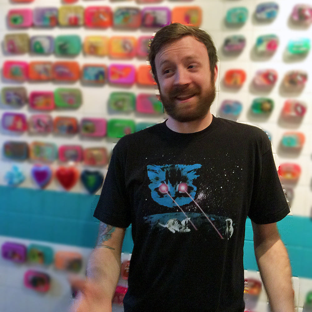 Man wearing a black t-shirt with a graphic design in front of a colorful wall.