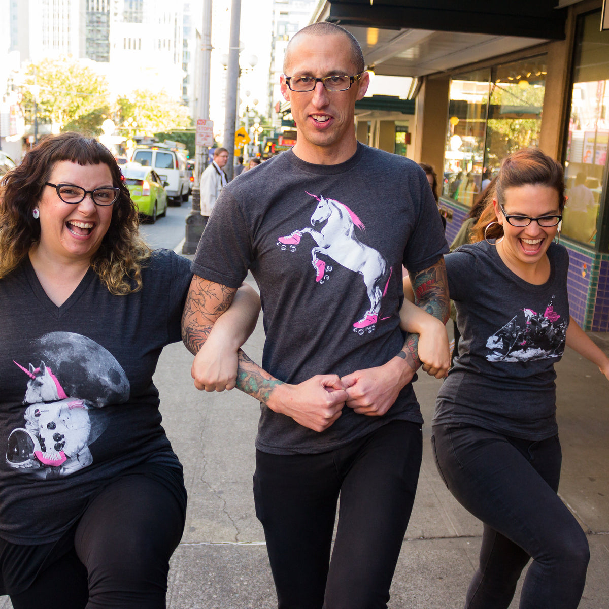 Three people walking down a city street wearing t-shirts with screenprinted unicorns wearing roller skates. 
