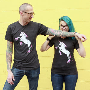 Two people wearing black t-shirts with a unicorn wearing roller skates graphic against a yellow wall.