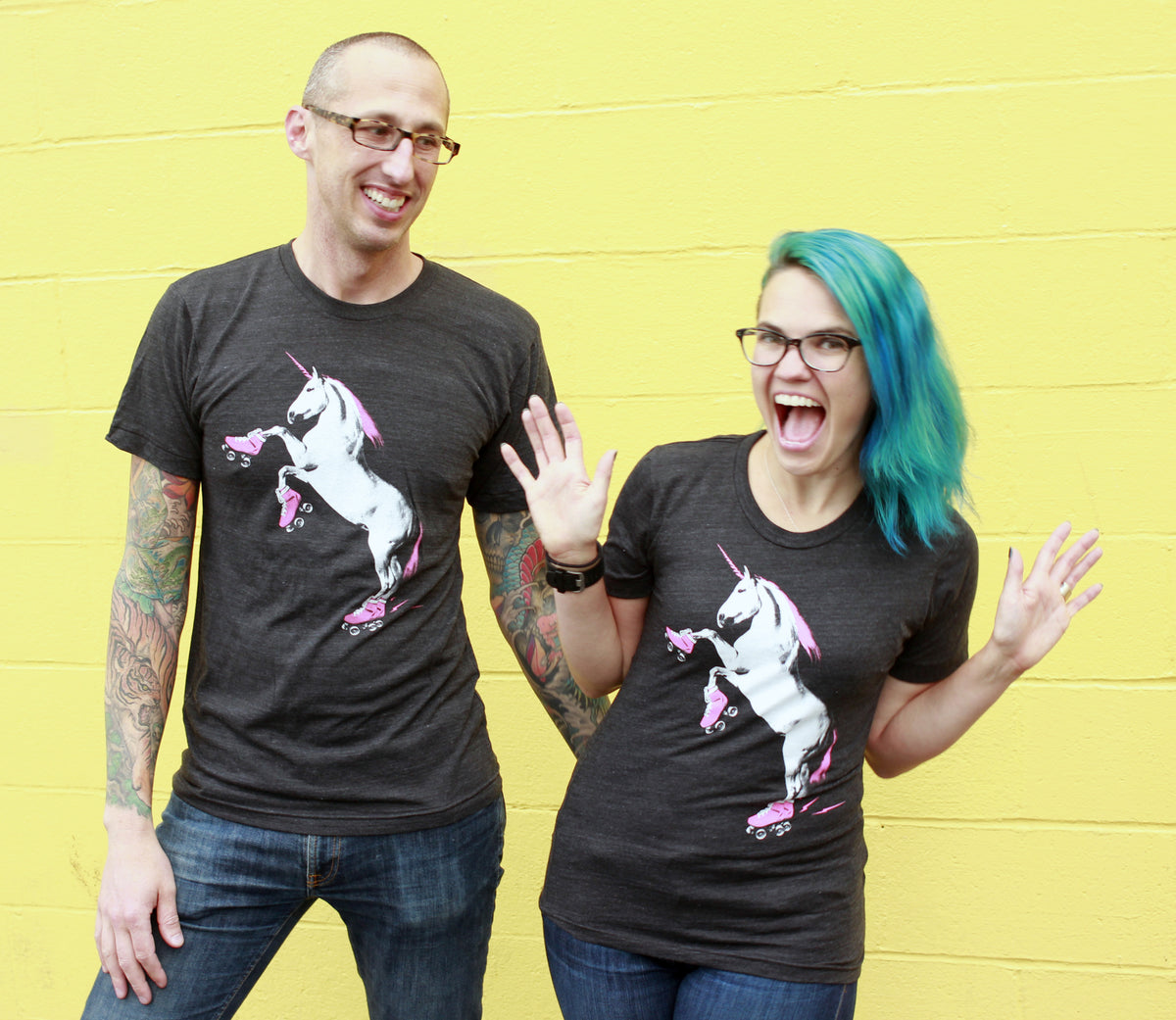 Two people wearing black t-shirts with a unicorn wearing roller skates graphic against a yellow background. 