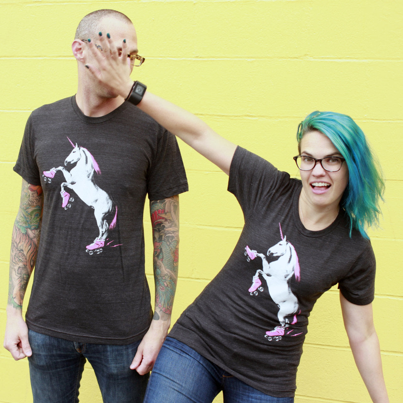 Two people wearing black t-shirts with a unicorn graphic against a yellow wall.