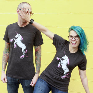 Two people wearing black t-shirts with a unicorn graphic against a yellow wall.