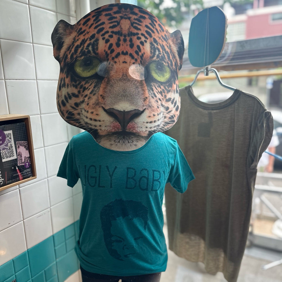 Mannequin wearing a leopard head mask & a heather teal Ugly Baby logo shirt.