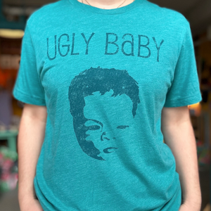 Person wearing a teal t-shirt with 'UGLY BABY' text and graphic design.