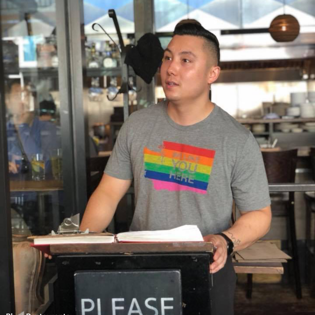 Person wearing a gray t-shirt with a rainbow flag design in a restaurant setting