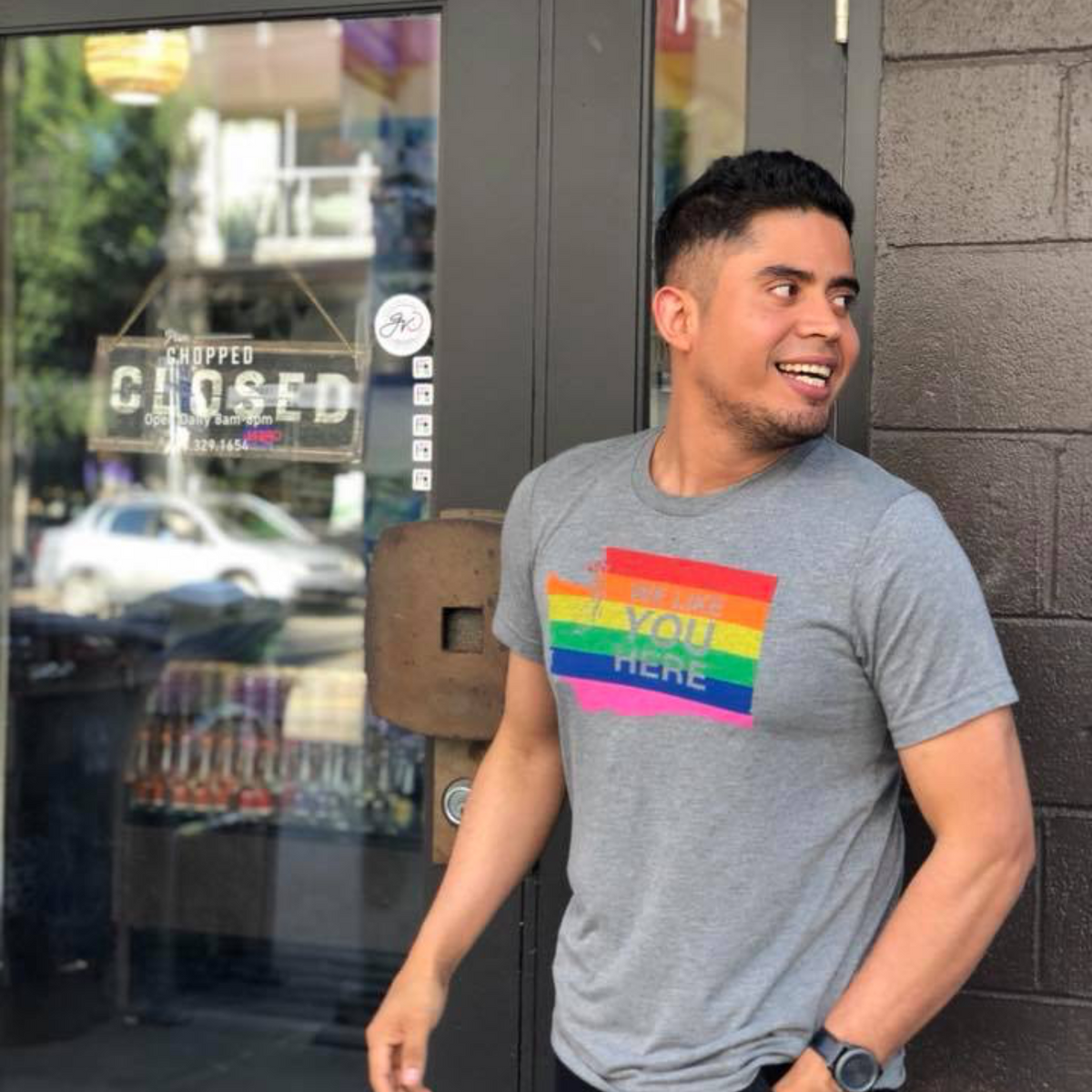 Man wearing a gray t-shirt with a rainbow design standing outside a building.