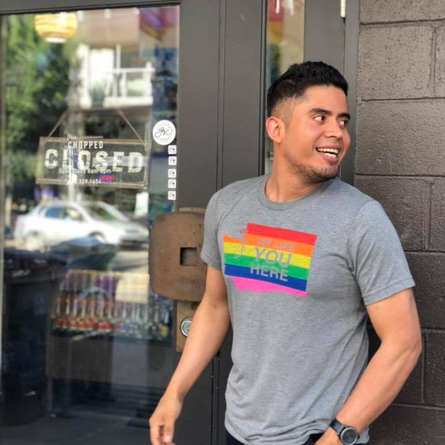 Man wearing a gray t-shirt with a rainbow design standing outside a building.