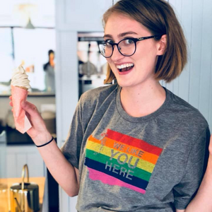 Person wearing a gray t-shirt with a rainbow flag design, holding ice cream in a kitchen.