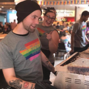 Person wearing a rainbow-colored shirt with text in a casual setting, possibly a restaurant.