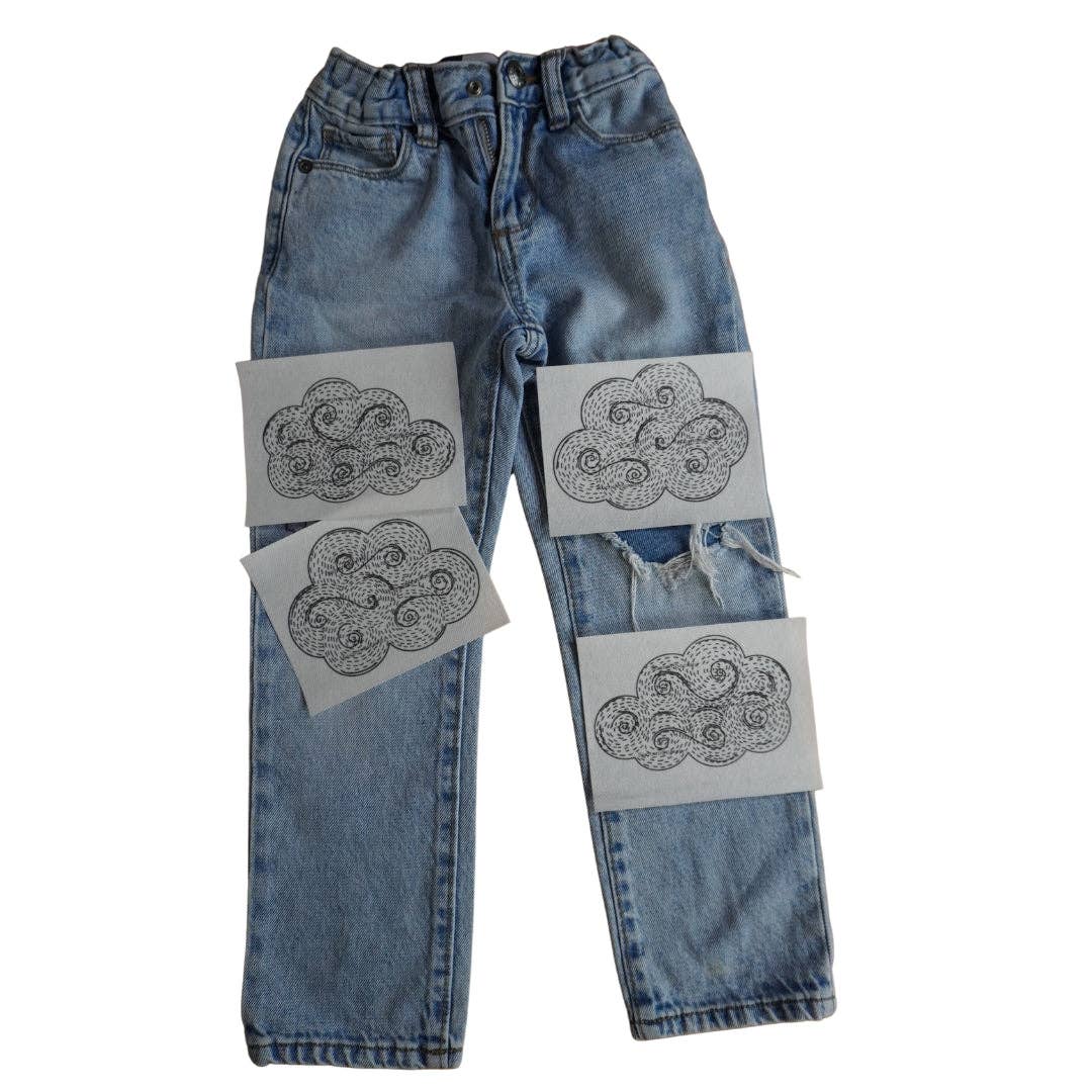 Cloud-shaped visible mending patterns on a pair of jeans against a white background. 