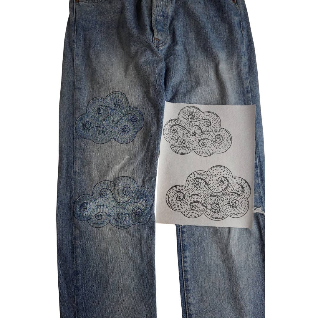 A pair of jeans with stitched up cloud patterns on one side and just the patterns on the other. 