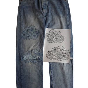 A pair of jeans with stitched up cloud patterns on one side and just the patterns on the other. 