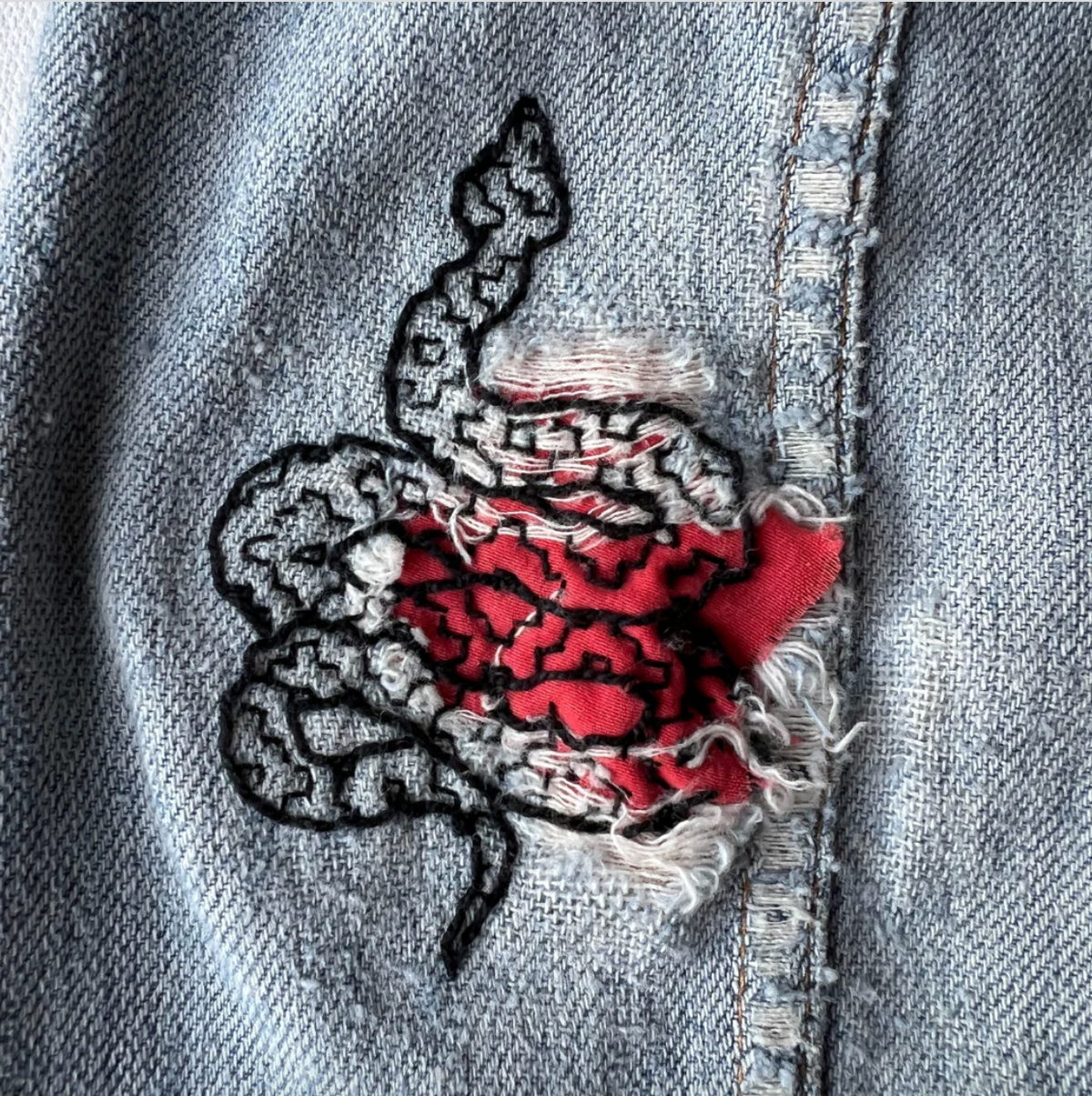 Embroidered snake on denim with a red patch. 