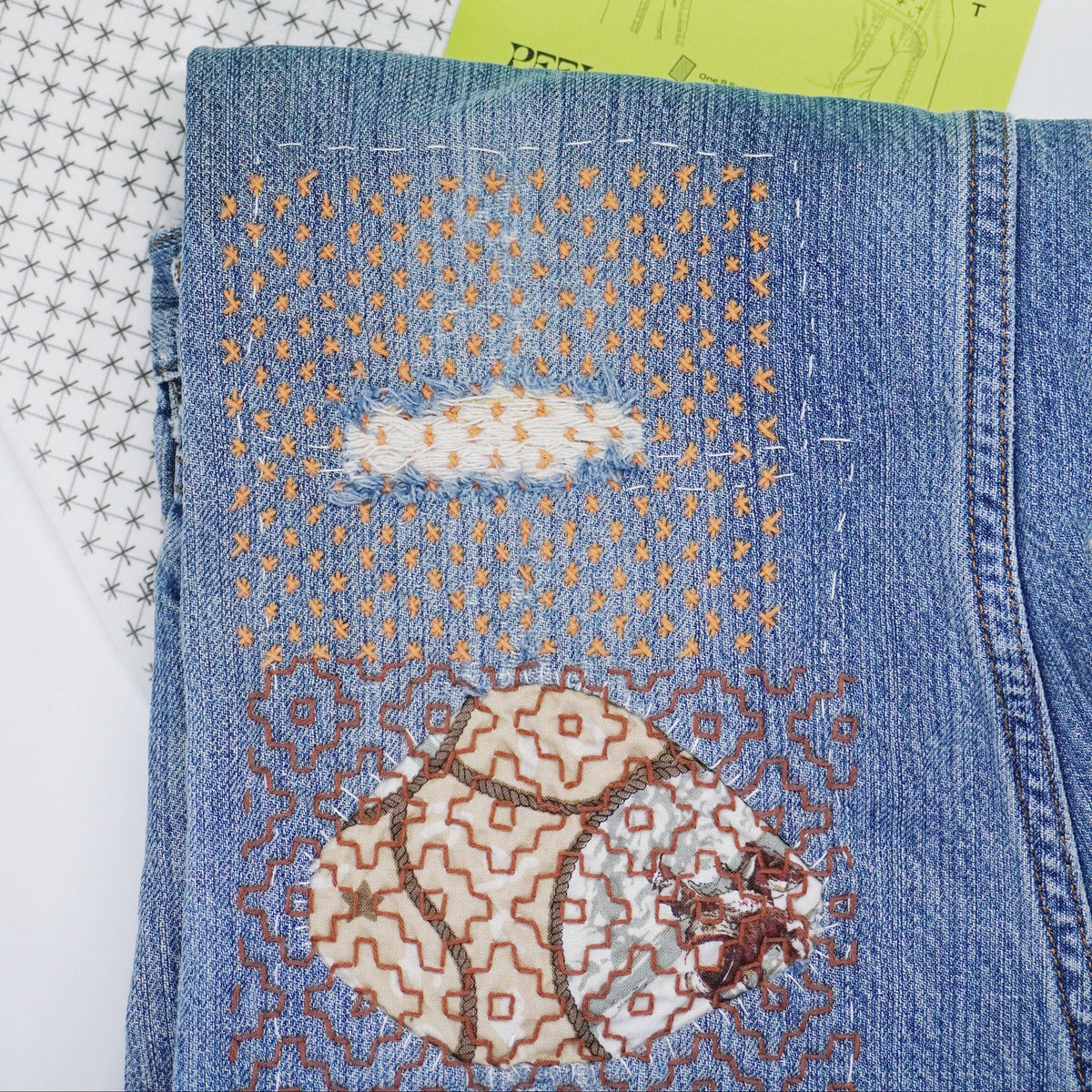 Stitched up example of visible mending on a pair of jeans with a stick and stitch pattern in the background. 