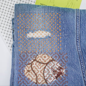 Stitched up example of visible mending on a pair of jeans with a stick and stitch pattern in the background. 