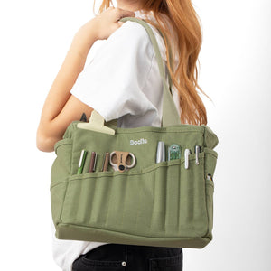 Person holding a green bag with various compartments on a white background