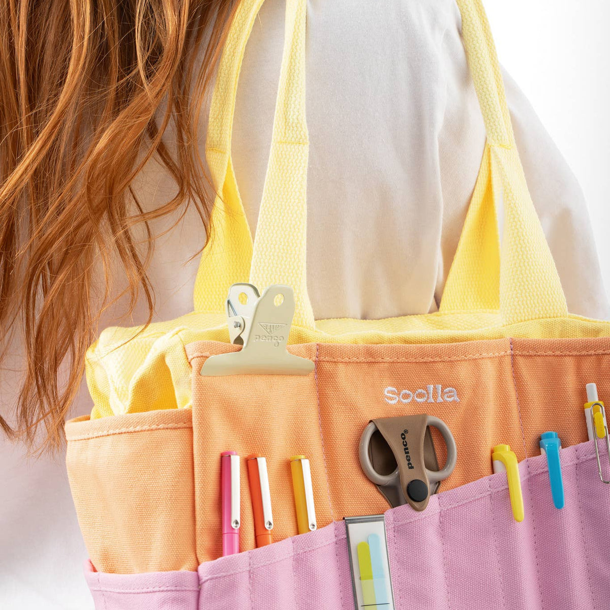Person holding a yellow and pink organizer with stationery items on a white background