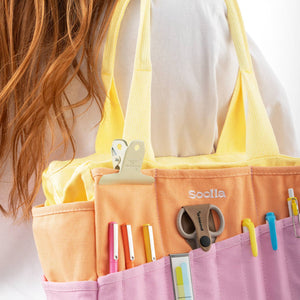Person holding a yellow and pink organizer with stationery items on a white background