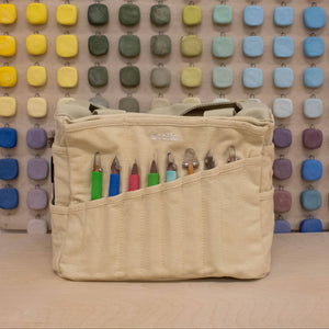 Beige bag with colorful items against a multicolored square patterned wall.