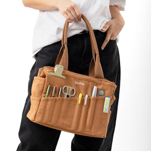 Person holding a brown tool bag with various tools on a white background