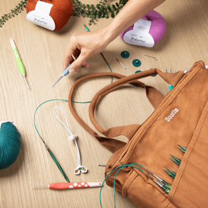Brown craft bag with knitting tools and yarn on a wooden surface