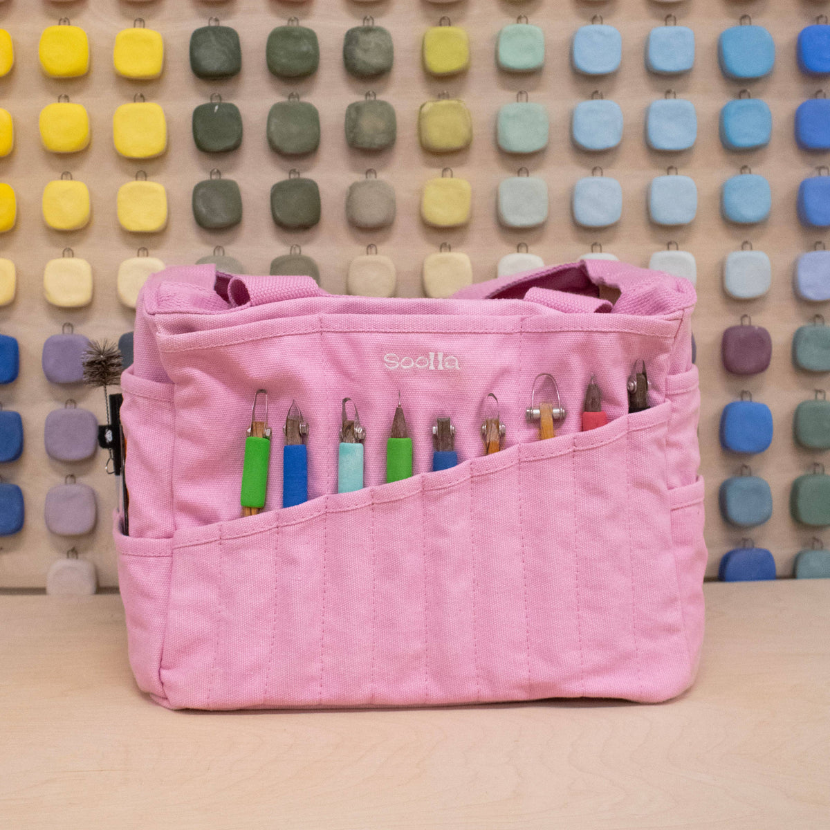 Pink project bag with colorful pens against a multicolored square patterned wall.