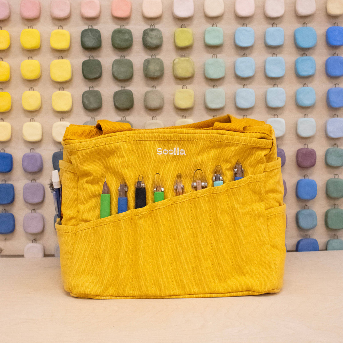 Yellow bag with stationery items against a colorful geometric wall.