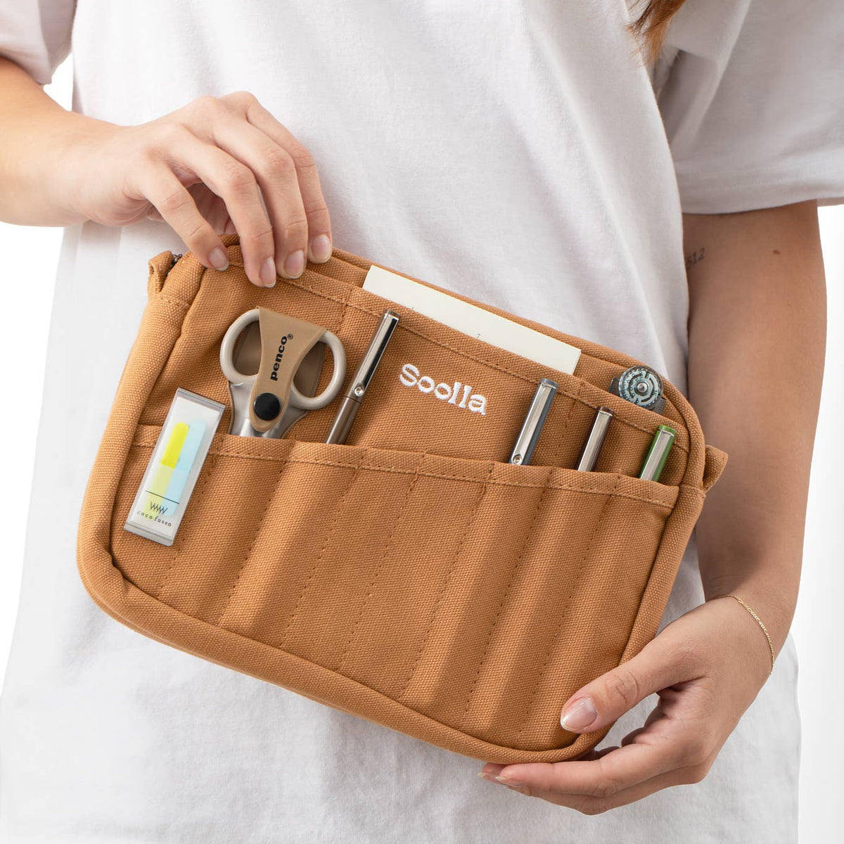 Person holding a brown tool pouch with various tools inside on a white background