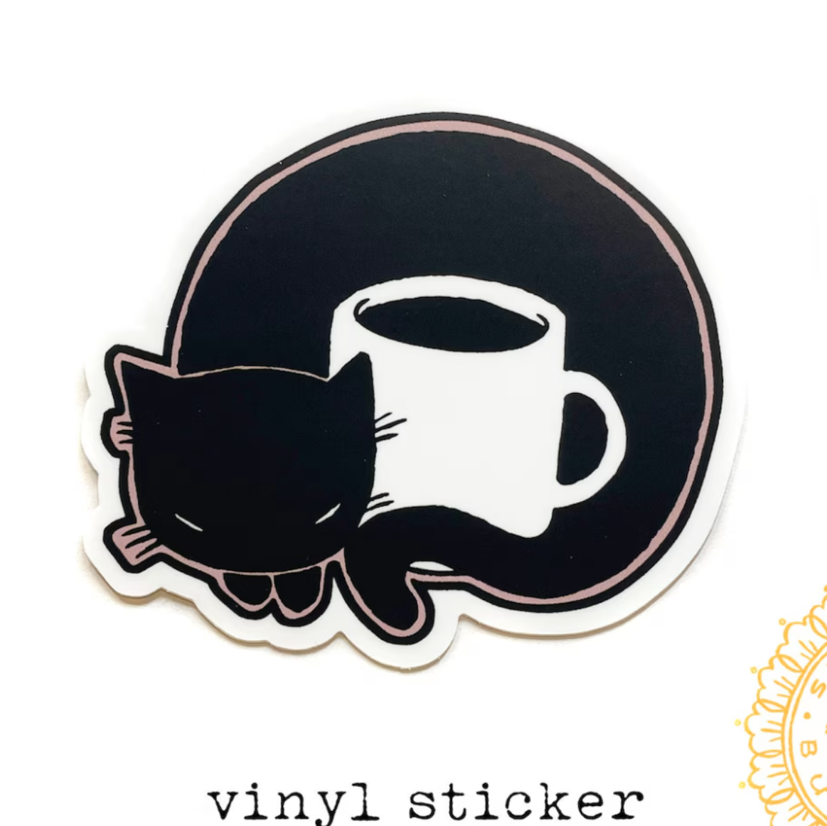 Vinyl sticker of a cat curled around a mug with a ruler for scale on a white background