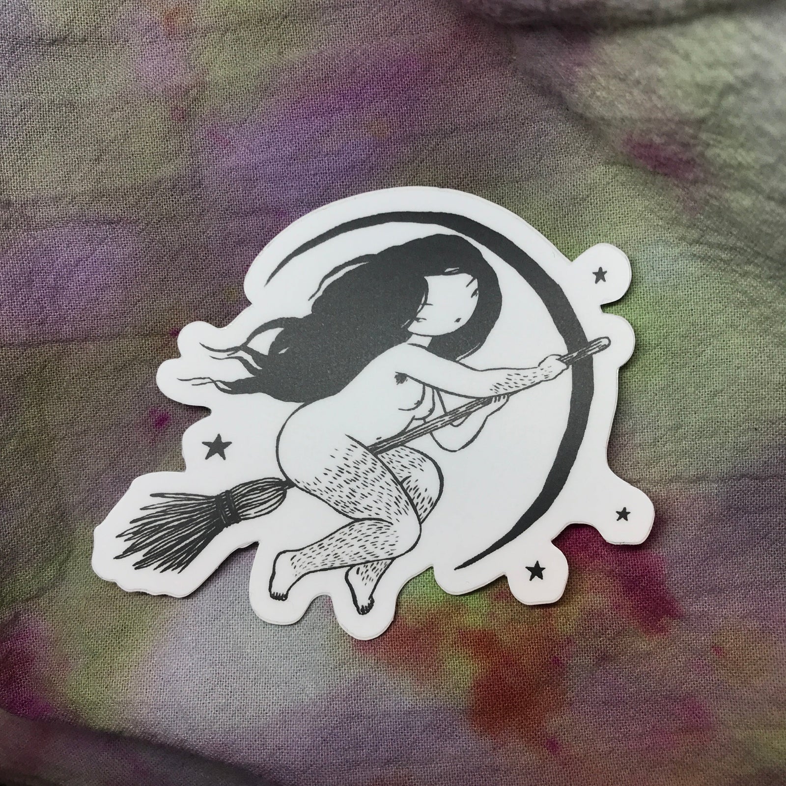 A sticker of a naked witch with hairy legs and armpits riding a broom with a crescent moon and stars in the background