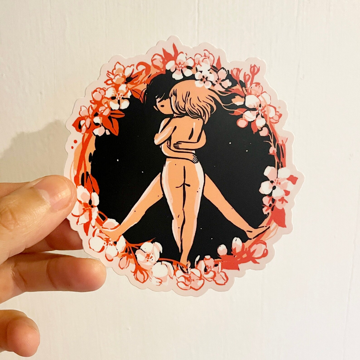 A sticker of two naked people forming a peace sign with a ring of flowers around them. 