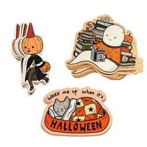 Three Halloween-themed stickers on a plain white background: a pumpkin character in a witch outfit, a ghost surrounded by books, and a cat sleeping in an orange Halloween bed with the text 'Wake me up when it's HALLOWEEN'.