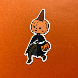 A die-cut sticker featuring a cute cartoon pumpkin character dressed as a vampire, holding a small jack-o'-lantern bucket, shown on a textured orange background.