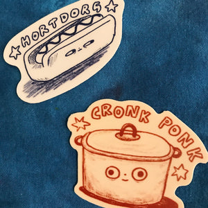 Two die-cut stickers displayed on a textured blue fabric background. The top sticker features a cute hand-drawn hot dog with the text 'HORTDORG' in black ink. The bottom sticker is a crock pot with a face and it says 'CRONK PONK" 