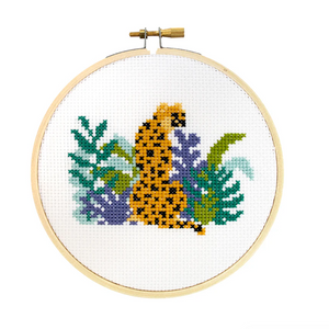 Cross-stitched cheetah design on white fabric in a wooden hoop. 