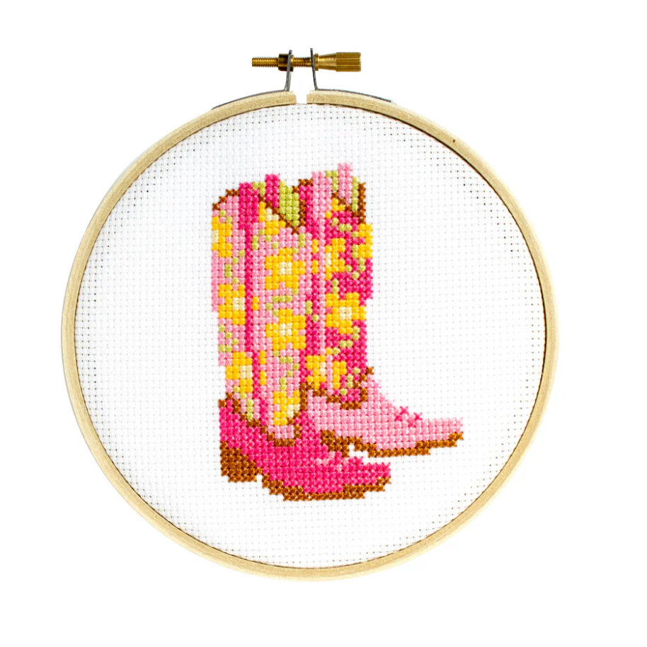 Cross-stitched pink cowboy boots in a wooden hoop on a white background