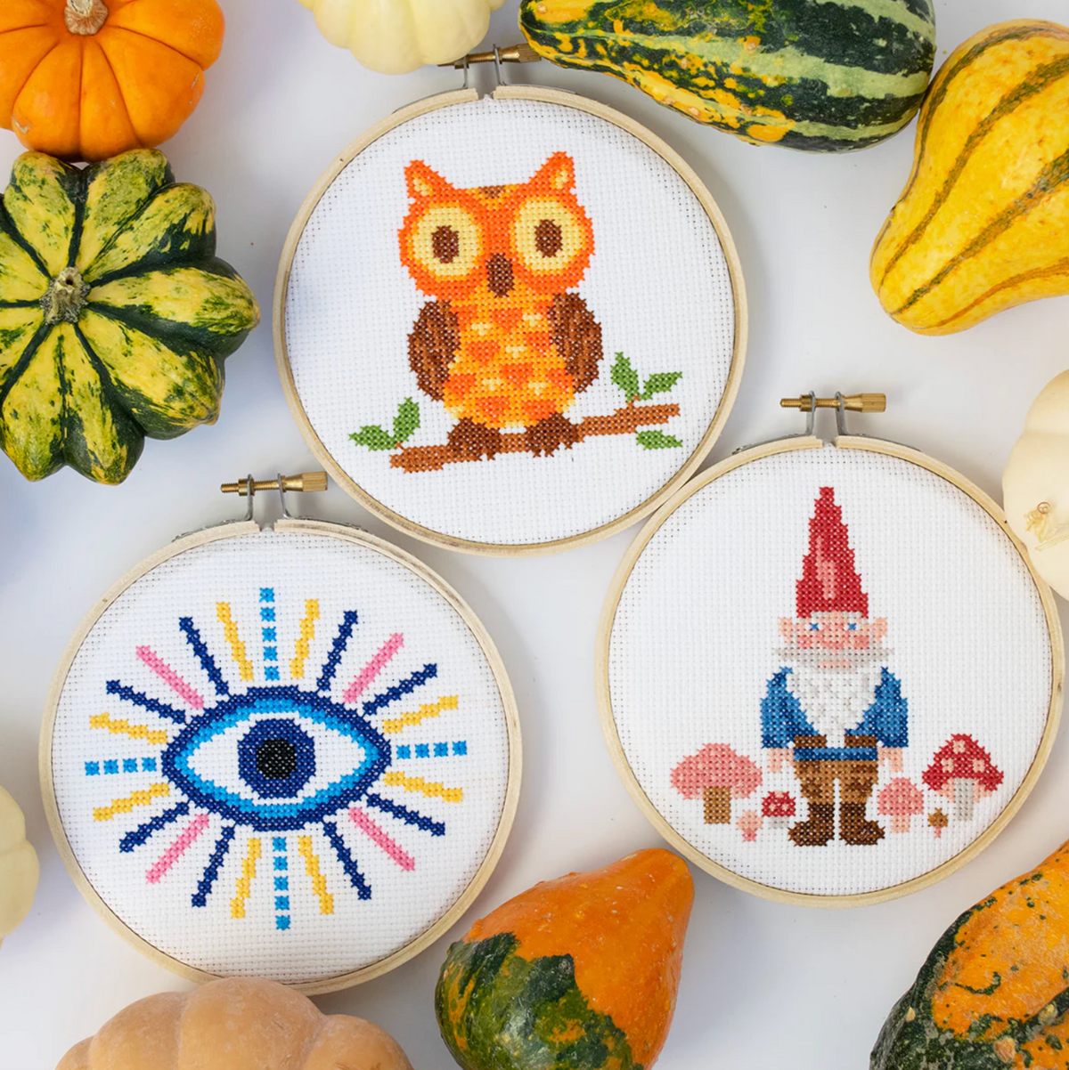 Three cross-stitching hoops with an owl, gnome and evil eye surrounded by pumpkins.
