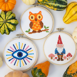 Three cross-stitching hoops with an owl, gnome and evil eye surrounded by pumpkins.