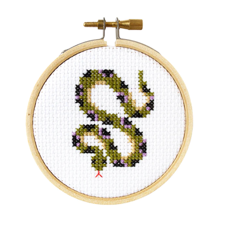 A cross stitch kit with a completed snake design, mounted in a 3 inch embroidery hoop.