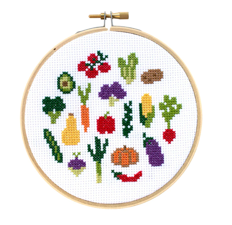 A finished cross-stitch featuring a grouping of vegetables like eggplant, potato, corn, carrots, and broccoli all on a white background. 