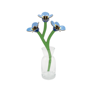 Stem of forget-me-nots made out of cardboard in a small glass vase. 
