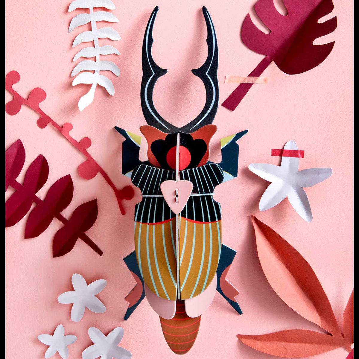 Cardboard sculpture of a giant stag beetle on a ink wall with various pink and white leaves. 