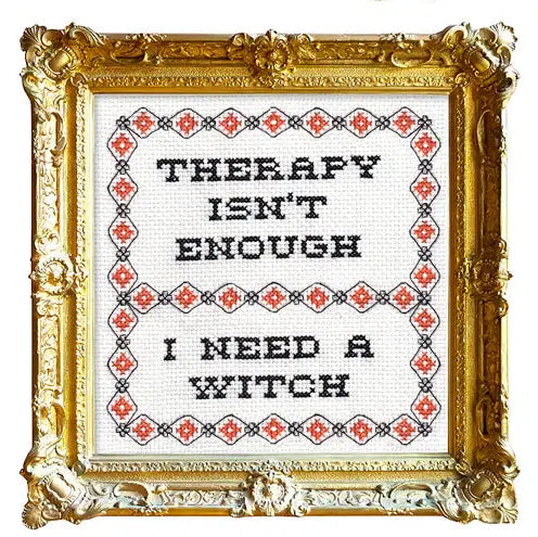 Gold framed cross stitch piece with text that reads "THERAPY ISN'T ENOUGH/I NEED A WITCH" with a patterned border. 